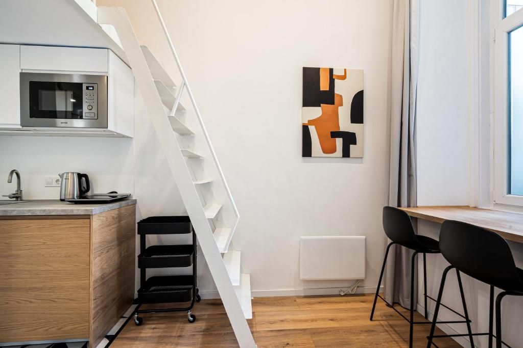 Cocina moderna con microondas, hervidor y un carrito negro. Una escalera conduce a un comedor con dos sillas negras.