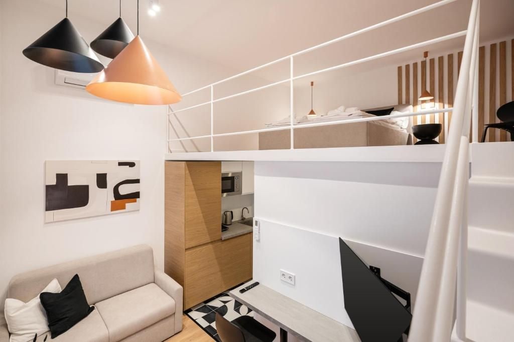 Un espacio habitable compacto con sofá, kitchenette y un entrepiso con cama.