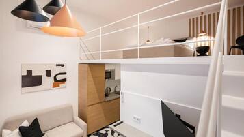 Un espacio habitable compacto con sofá, kitchenette y un entrepiso con cama.