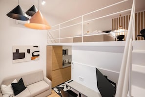 Un espacio habitable compacto con sofá, kitchenette y un entrepiso con cama.