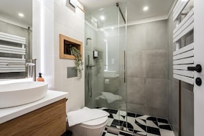 Ein modernes Badezimmer mit einer ein Glasfachraum-Dusche, einem weißen Waschbecken und einem schwarz-weißen gemusterten Boden.