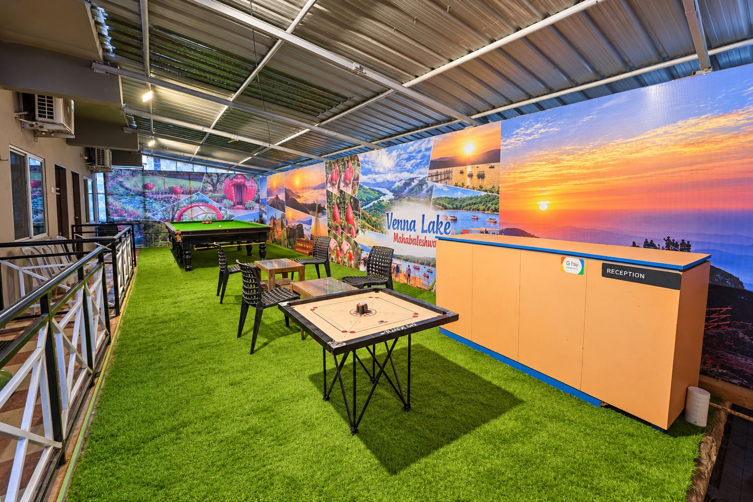 Un espace de loisirs intérieur comprenant une table de billard, une piscine et une table de snooker, agrémenté d’une fresque représentant un coucher de soleil sur un lac.
