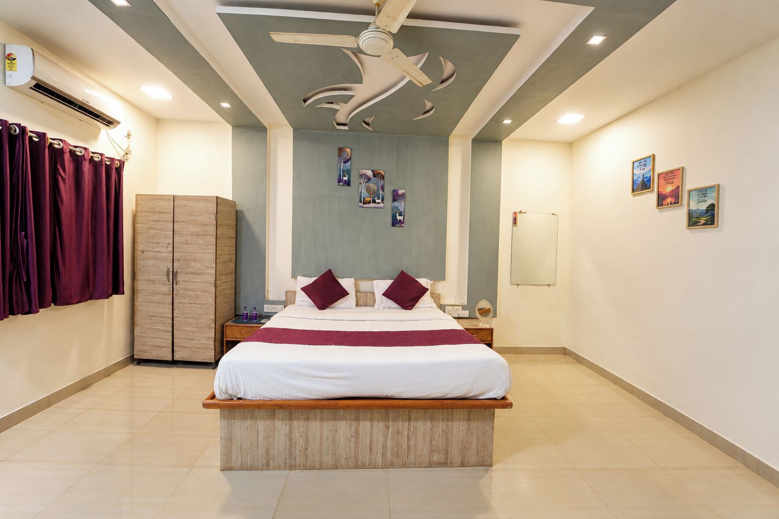 A hotel room with a bed, a wardrobe, a ceiling fan, and artwork on the walls.