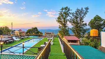A rooftop pool area with a view of the mountains, a restaurant, and a water tank.