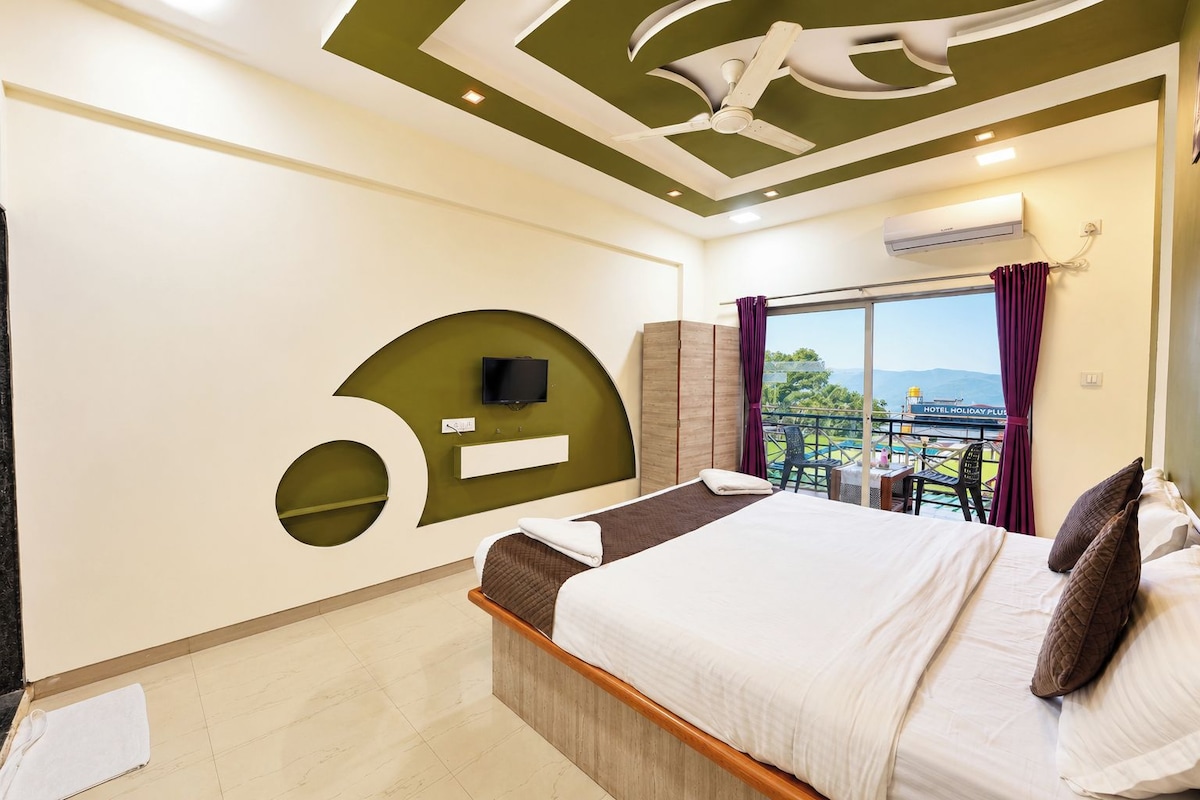 A hotel room with a bed, a TV, a balcony with a view, and a ceiling fan.