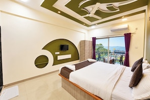 A hotel room with a bed, a TV, a balcony with a view, and a ceiling fan. - Mist Valley Resort (Mahabaleshwar)