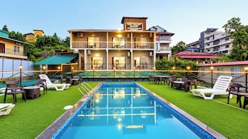 Hotel com piscina, área de estar ao ar livre e placa indicando quartos disponíveis.