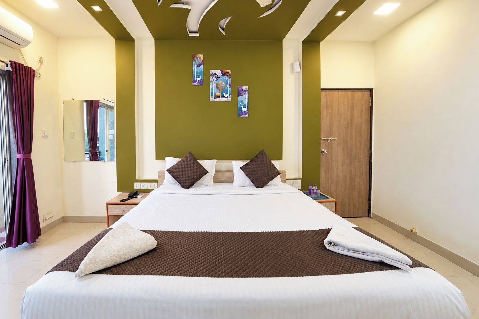 Quarto de hotel com uma cama grande, mesa de cabeceira, espelho, porta e obras de arte na parede.