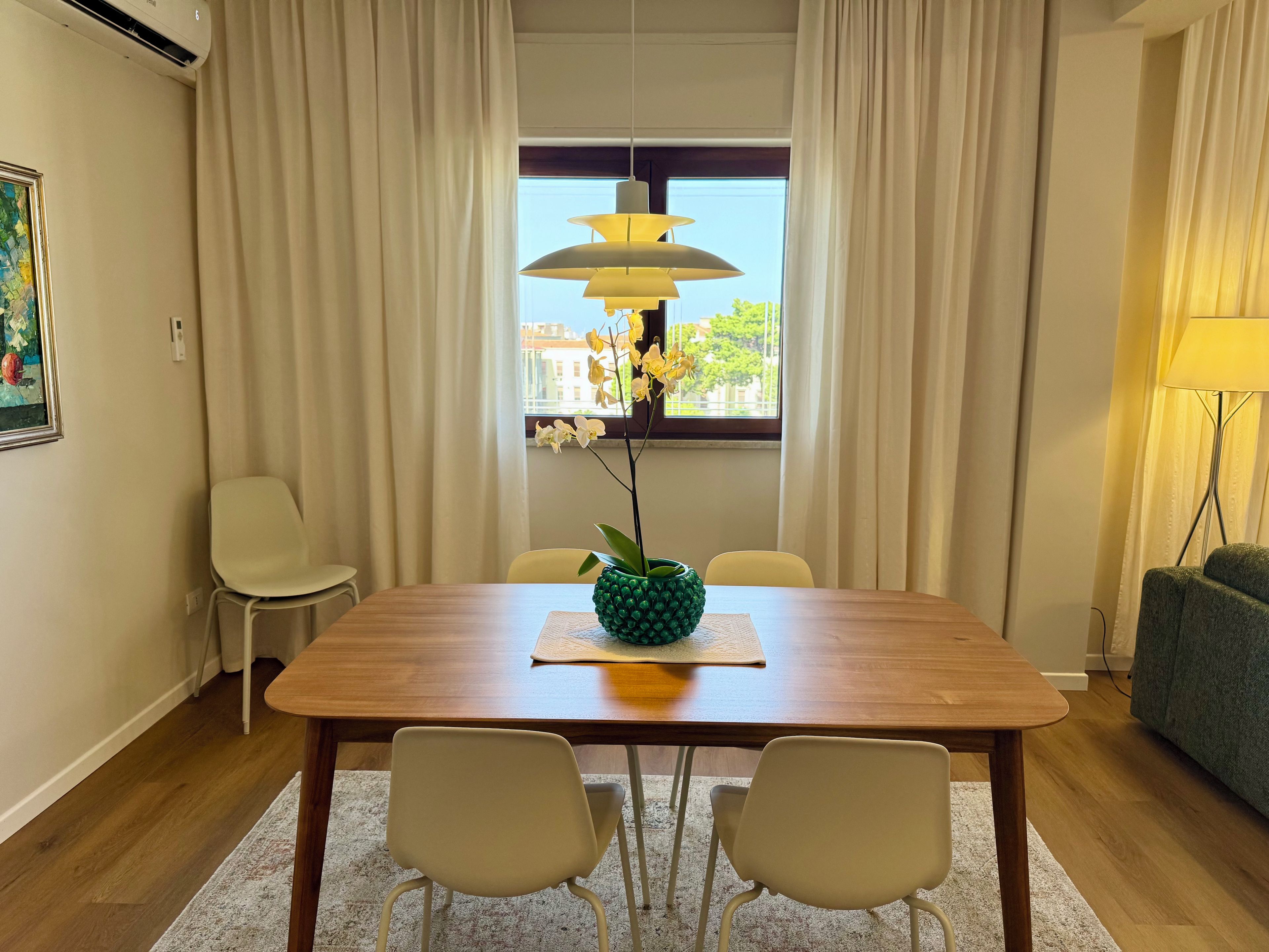 Un coin repas avec une table en bois, deux chaises, un vase de fleurs et une fenêtre avec des rideaux.