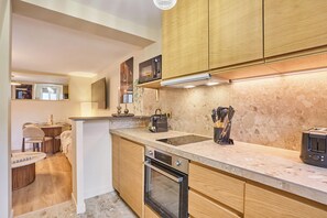 A modern kitchen with wooden cabinets, a built-in oven, and a countertop with a coffee maker and utensils. - Spacious air-conditioned studio in Le Marais, central Paris (Paris)