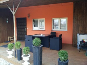 An outdoor seating area with a table and chairs, surrounded by potted plants, against an orange wall. - Holiday Home in Ketzin With Swimming Pool (Ketzin/Havel)