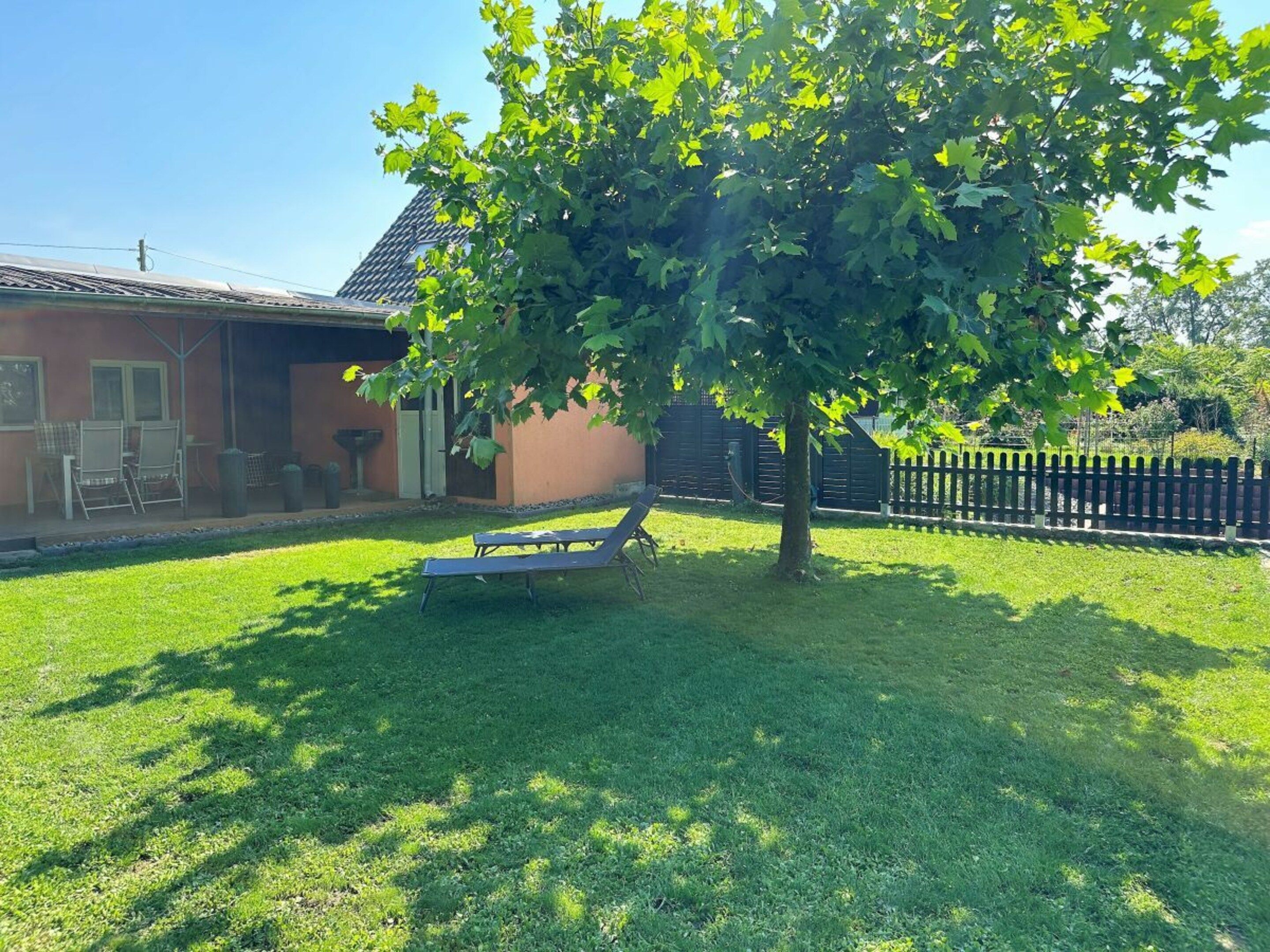 Il s’agit d’une propriété résidentielle dotée d’une pelouse, d’une terrasse avec des chaises, d’un arbre et d’une clôture.