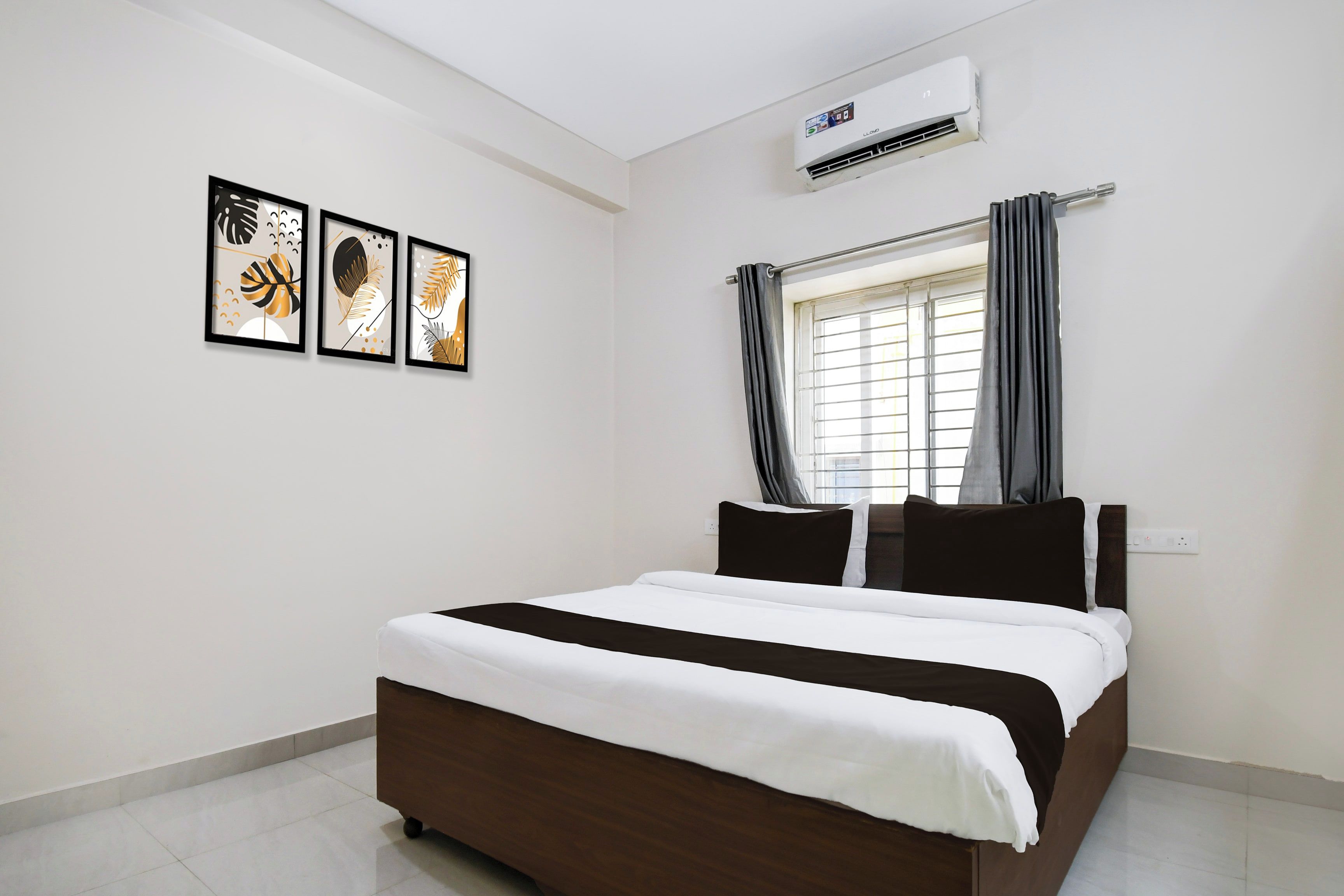 Un dormitorio con cama, unidad de aire acondicionado, ventana con cortinas y tres obras de arte enmarcadas en la pared.