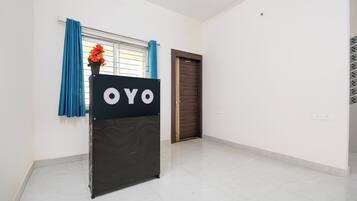 A room with a black sign reading 'OYO' on a stand, a window with blue curtains, a door, and a tiled floor.