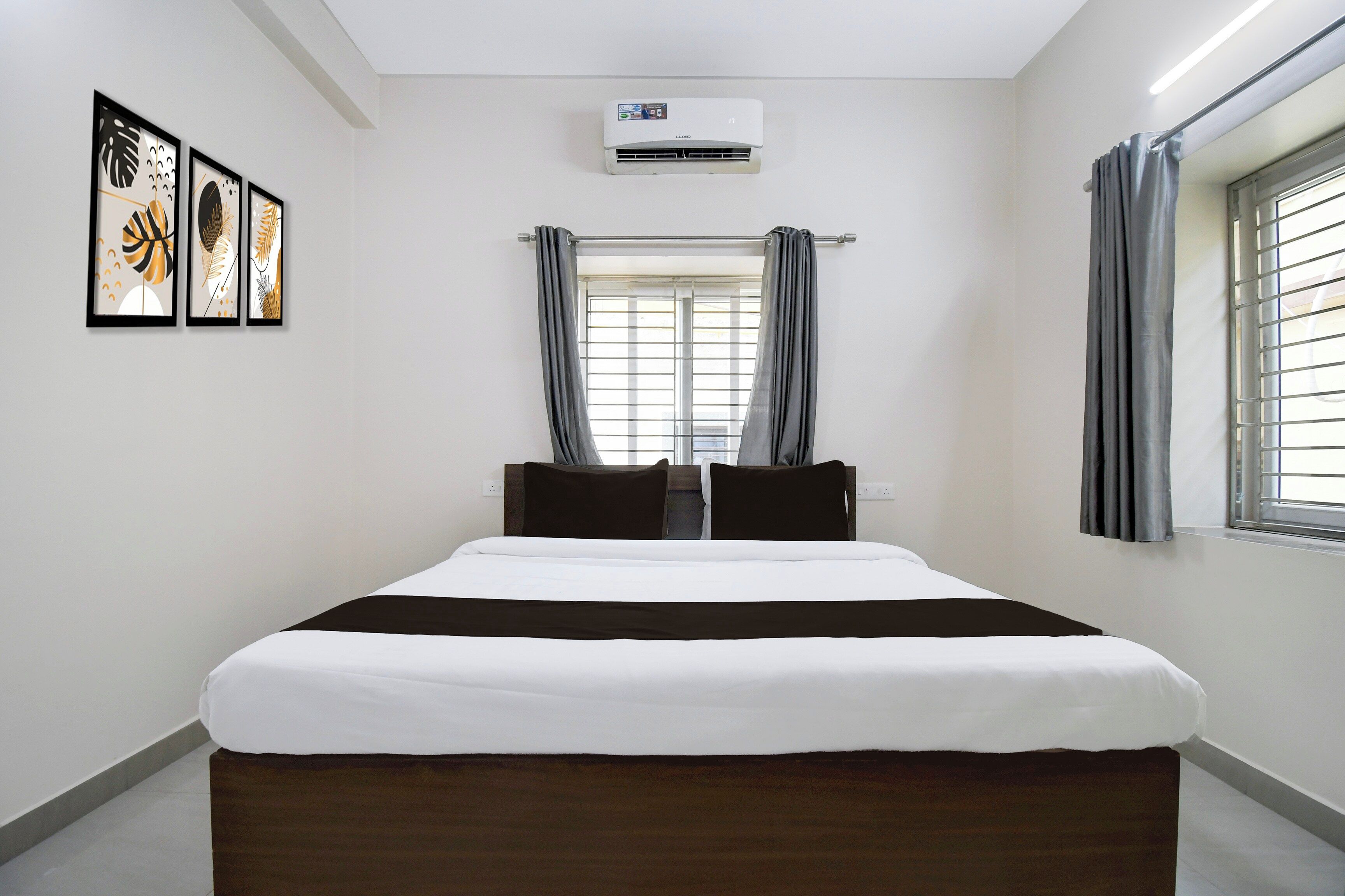 A hotel room with a bed, air conditioning unit, window with curtains, and wall art.