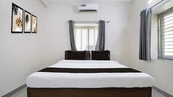A hotel room with a bed, air conditioning unit, window with curtains, and wall art.