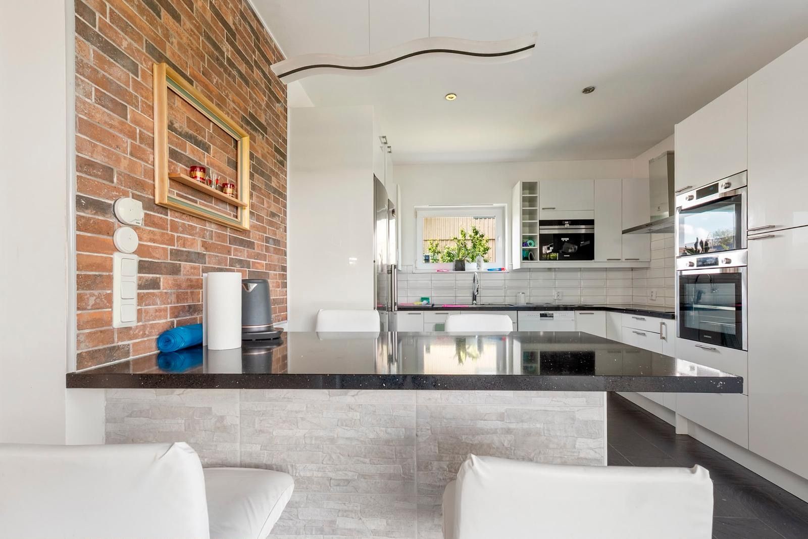 Una cocina moderna con una isla central, armarios blancos y una pared de ladrillo decorativa.