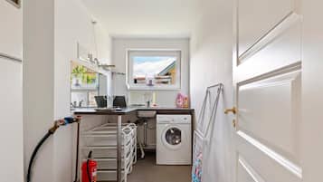 A compact laundry room with a washing machine, a sink, a drying rack, and a fire extinguisher.