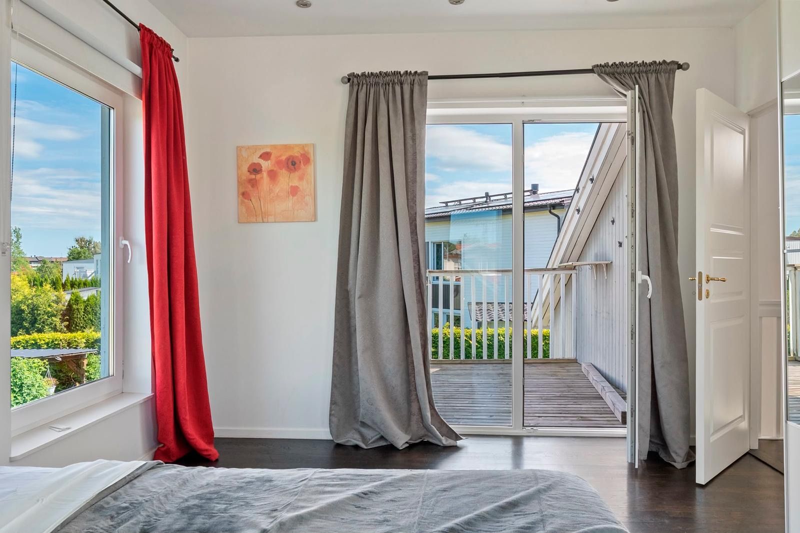 A bedroom with a large window, a sliding door to a balcony, and a bed with a gray cover.