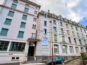 A multi-story building with a classic architectural style, featuring a central entrance with a staircase leading to the ground floor. - Apartment Near Mont-dore Centre (Mont-Dore)