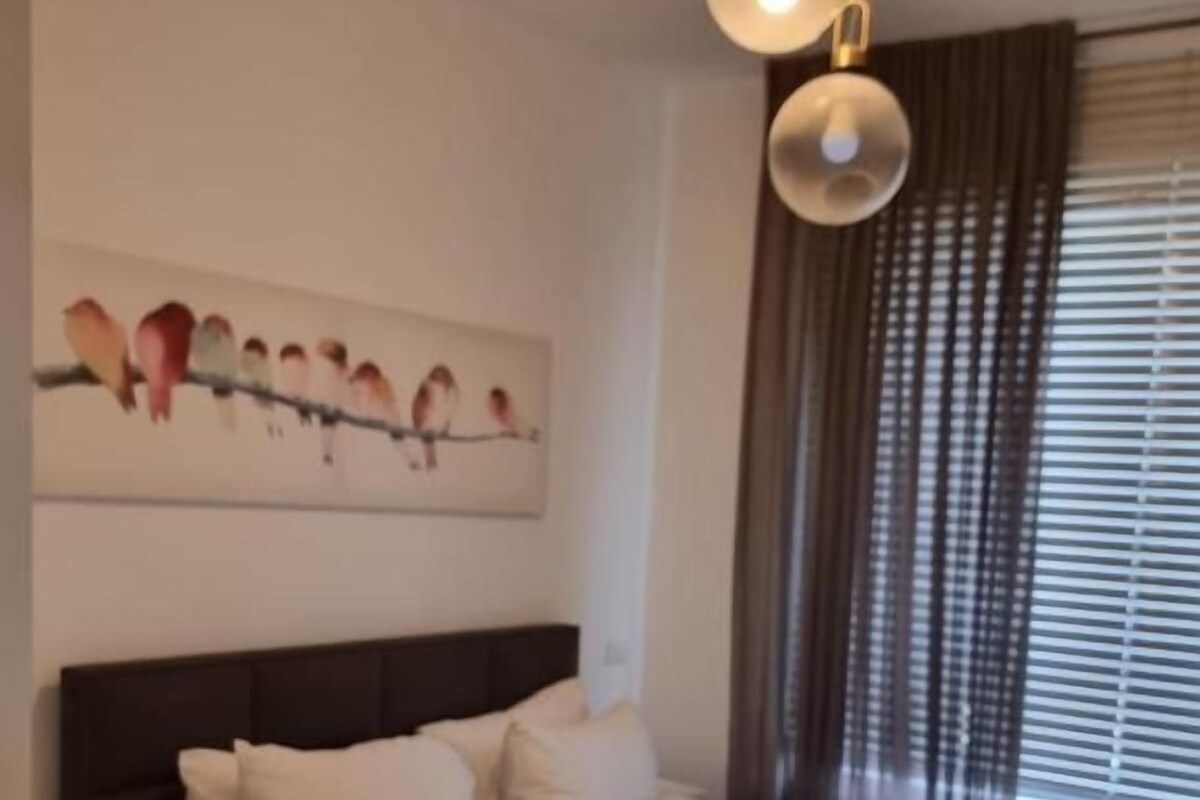 A bedroom with a large bed, a nightstand, a wall-mounted artwork, and a window with curtains.