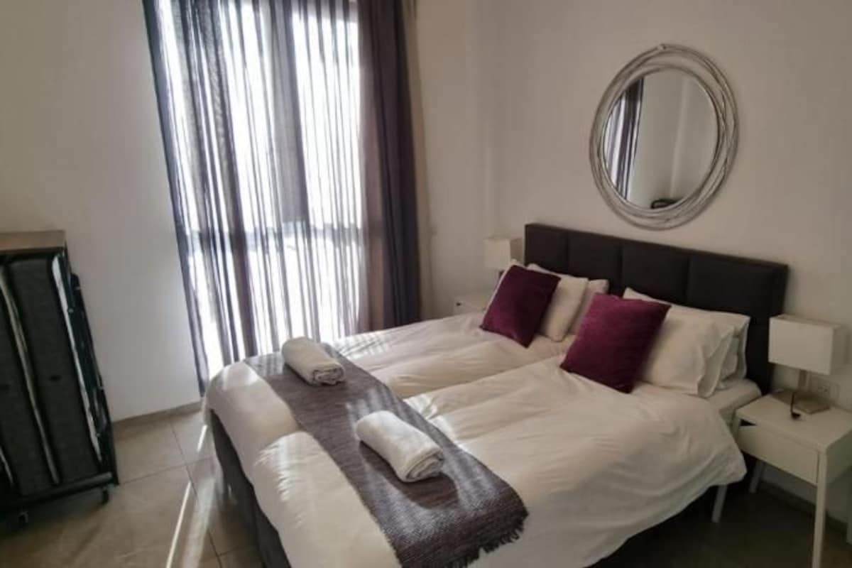 A hotel room with a bed, a nightstand, a mirror, and a window with curtains.