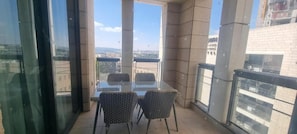 A balcony with a glass table and chairs, offering a view of the cityscape. - Jtowers G Royal Suites (Jerusalem)