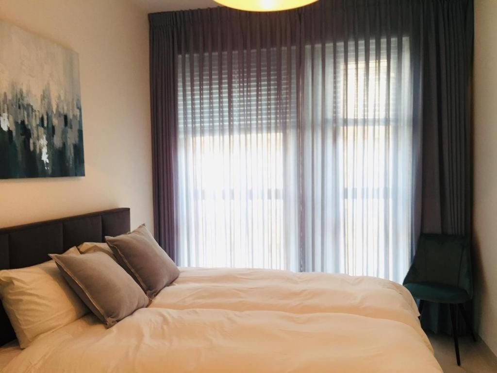 A hotel room with a large bed, a headboard, a painting on the wall, and a window with curtains.