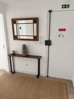 Ein Zimmer mit einem Holztischchen, einem Spiegel, einer Vase und einer Tür mit Notausgangsschildern.