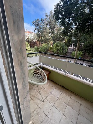 Ein Balkon mit einem weißen Stuhl, gefliestem Boden und Blick auf Bäume und Gebäude.