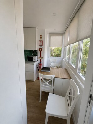 Eine kleine Küche mit weißen Schränken, einer Mikrowelle, einem Feuerlöscher und einem Fenster mit Blick auf Grünflächen.
