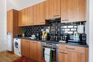 Una cocina moderna con armarios de madera, salpicadero de baldosas negras, electrodomésticos de acero inoxidable y lavadora.