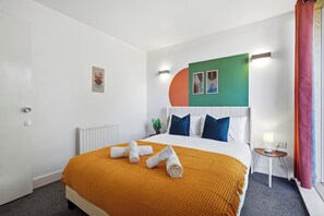 Een hotelkamer met een bed, een klein tafeltje, een lamp en een muur met kunst.