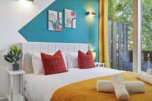 Een hotelkamer met een bed, kussens, een plant en kunst aan de muur.