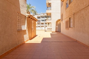 A corridor with tiled flooring, a gate, and a building with balconies in the background. - Casa del Sol Playa del los Locos Torrevieja (Torrevieja)
