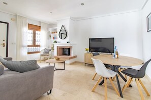 En moderne stue med sofa, et rundt spisebord med stole, pejs og et fladskærms TV.