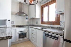 Een keuken met witte kasten, een roestvrijstalen afzuigkap, een inbouwoven, een vaatwasser en een granieten aanrecht.