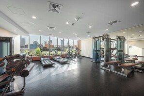 Uma academia com equipamentos de cardio, aparelhos de musculação e bancos.
