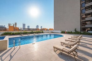 Ein Pool auf dem Dach mit Liegestühlen und einer Stadtansicht im Hintergrund.