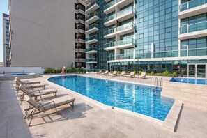 Piscina com espreguiçadeiras, cercada por um edifício moderno com várias varandas.