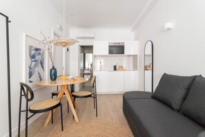 A modern living room with a dark sofa, a round dining table with chairs, and a kitchen area in the background. - Lapa Diplomatic Residence by Feel Lisbon (Lisbon)