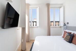 A bedroom with a bed, a TV mounted on the wall, and two windows with curtains. - Lapa Diplomatic Residence by Feel Lisbon (Lisbon)