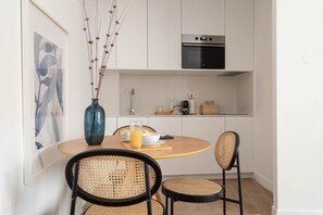 Eine moderne Küche mit Einbauofen, einem Esstisch mit Stühlen und einer Wandvase mit getrockneten Pflanzen.