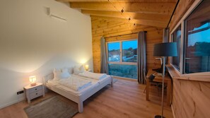 Quarto com cama, luminárias de cabeceira, escrivaninha e janela com cortinas.