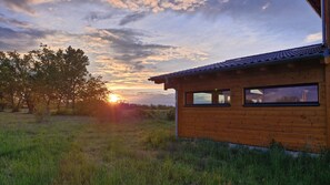 Eine Holzhütte mit einem Ziegeldach, umgeben von Gras und Bäumen, im Abendlicht.