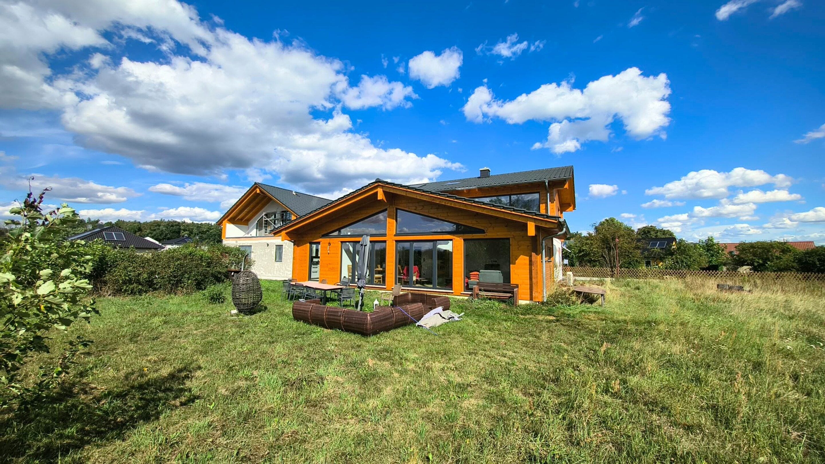 Uma casa moderna com uma grande janela de vidro, um deck de madeira e um gramado.