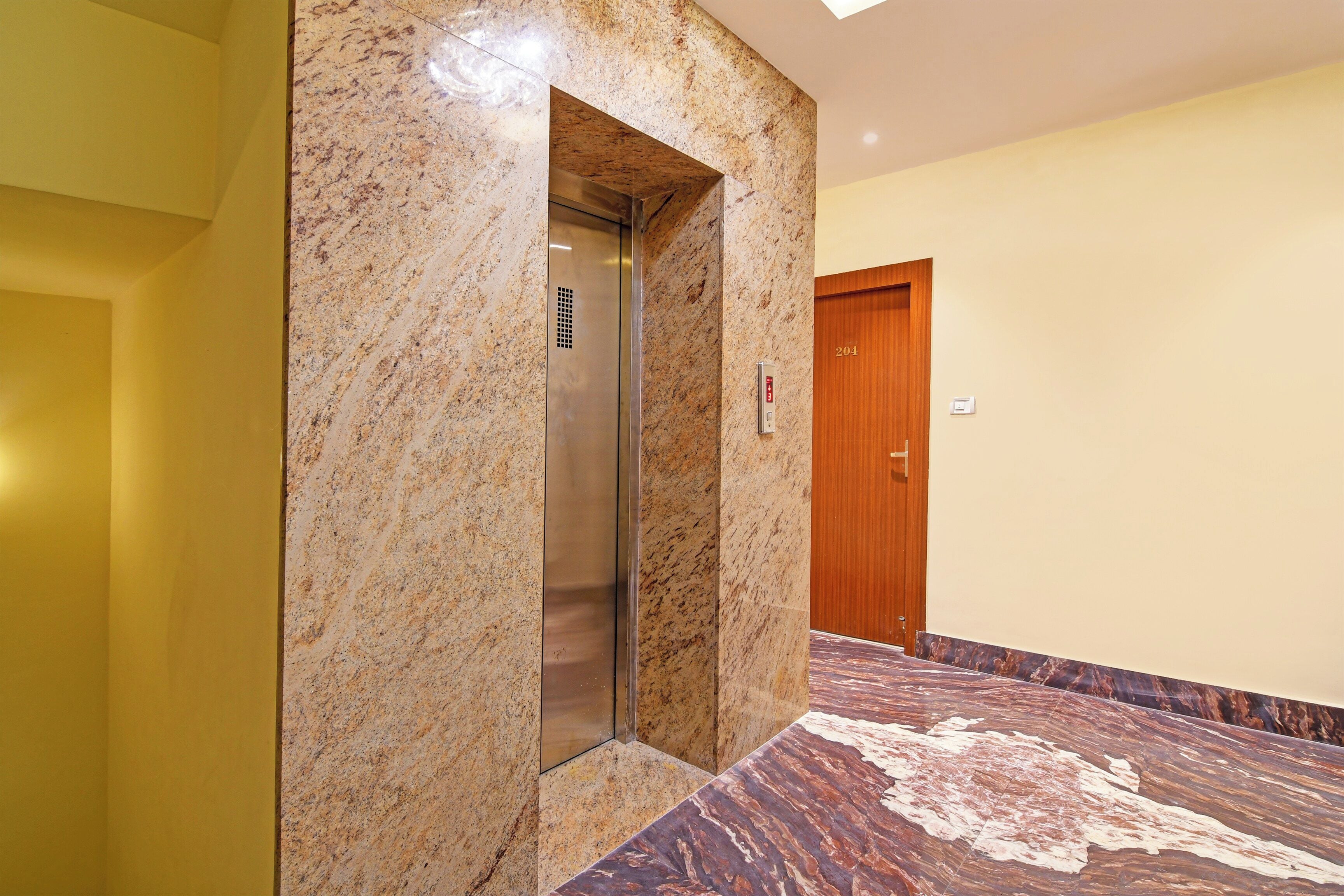 A marble elevator in a hallway with a wooden door and a patterned floor.