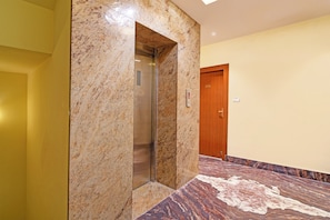 A marble elevator in a hallway with a wooden door and a patterned floor.