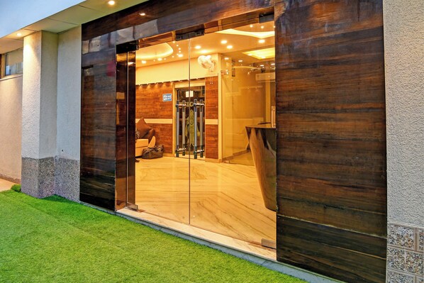 A modern building entrance with a glass door, a fire exit sign, and a visible interior with a staircase.
