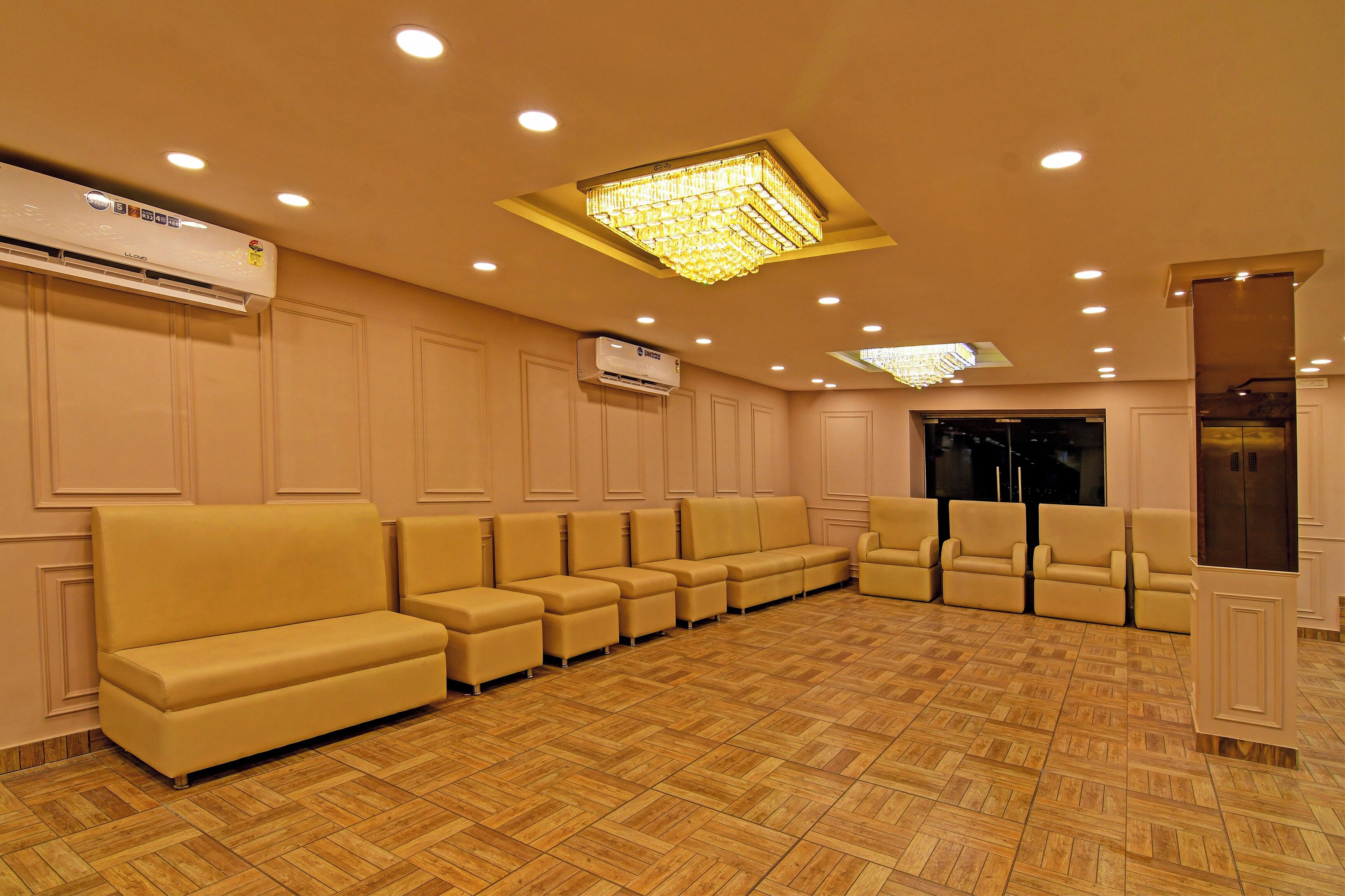 A hotel lobby with a row of beige sofas, a large chandelier, and an air conditioning unit on the wall.